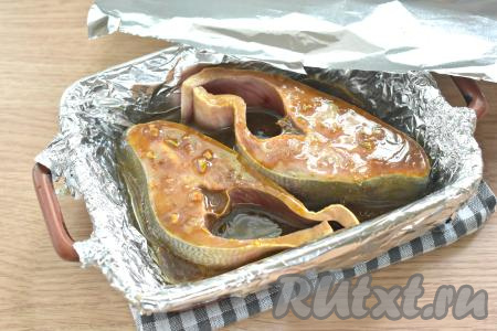 Жаропрочную форму застилаем фольгой. Выкладываем замаринованные стейки горбуши. Маринад тоже выливаем в форму. Сверху форму закрываем фольгой.